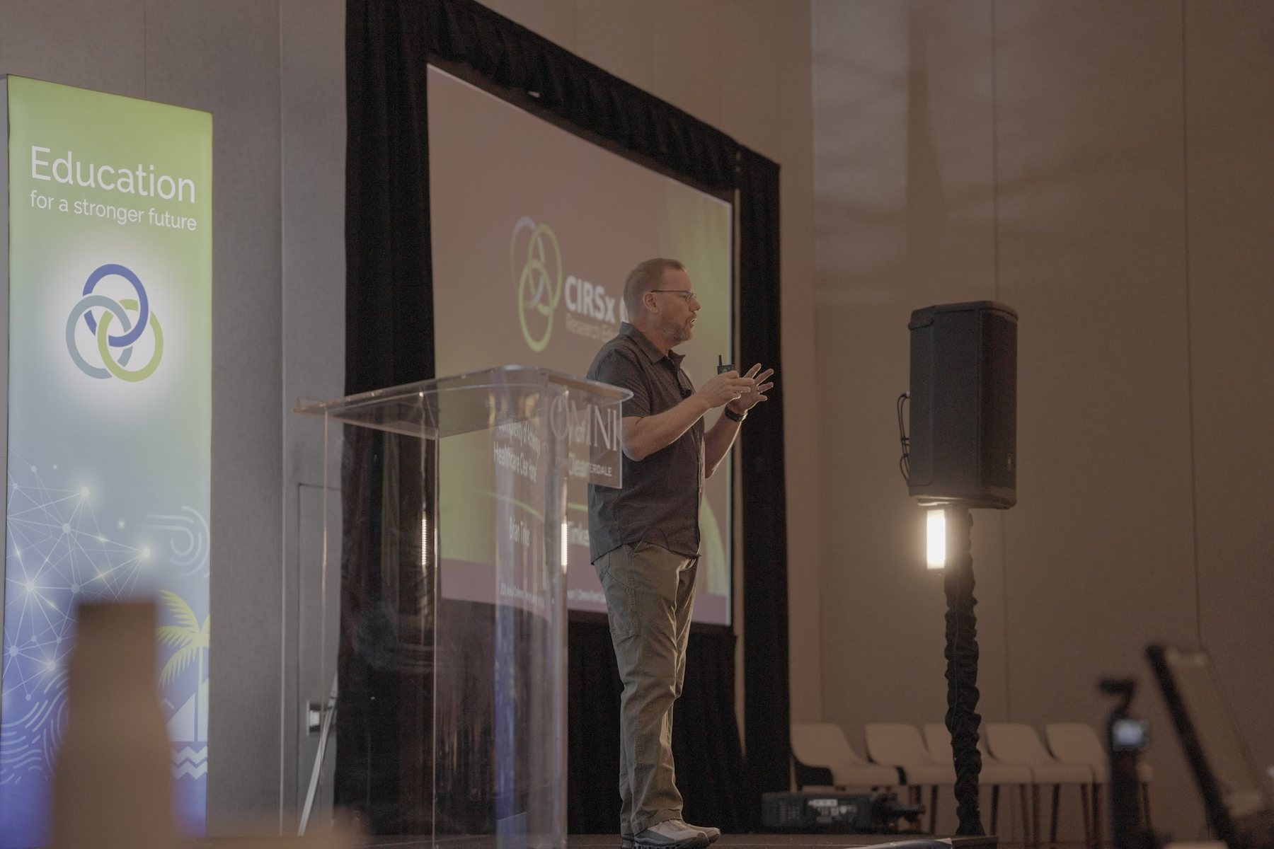 A presenter speaking at a podium beside a large screen
