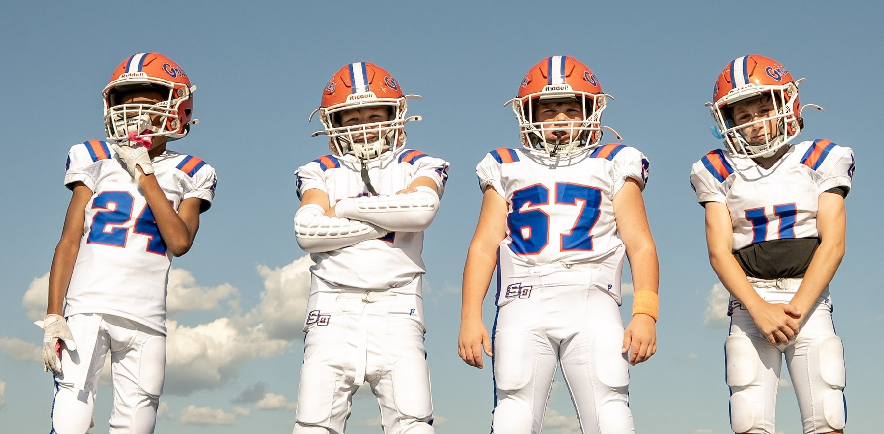 Four youth football players standing against a blue sky