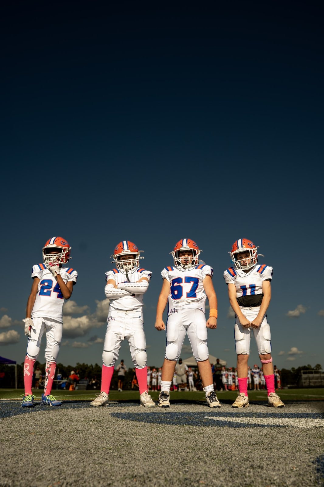 Four youth football players standing on the field under a deep blue sky