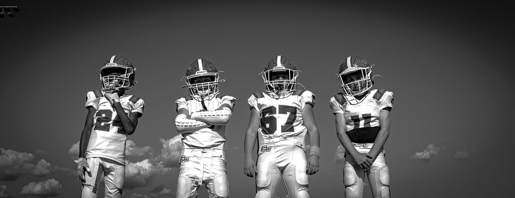 Black-and-white photo of youth football players standing against the sky