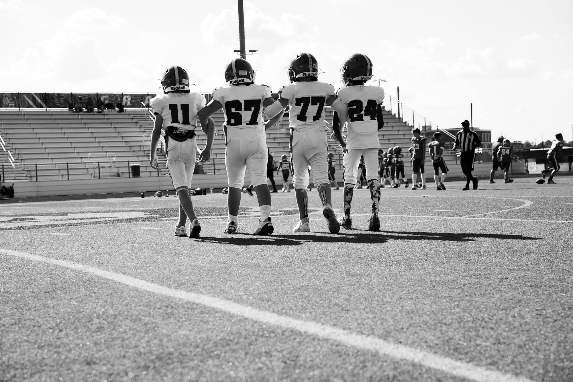 Black-and-white photo of two youth football captains walking arm in arm onto the field, seen from behind