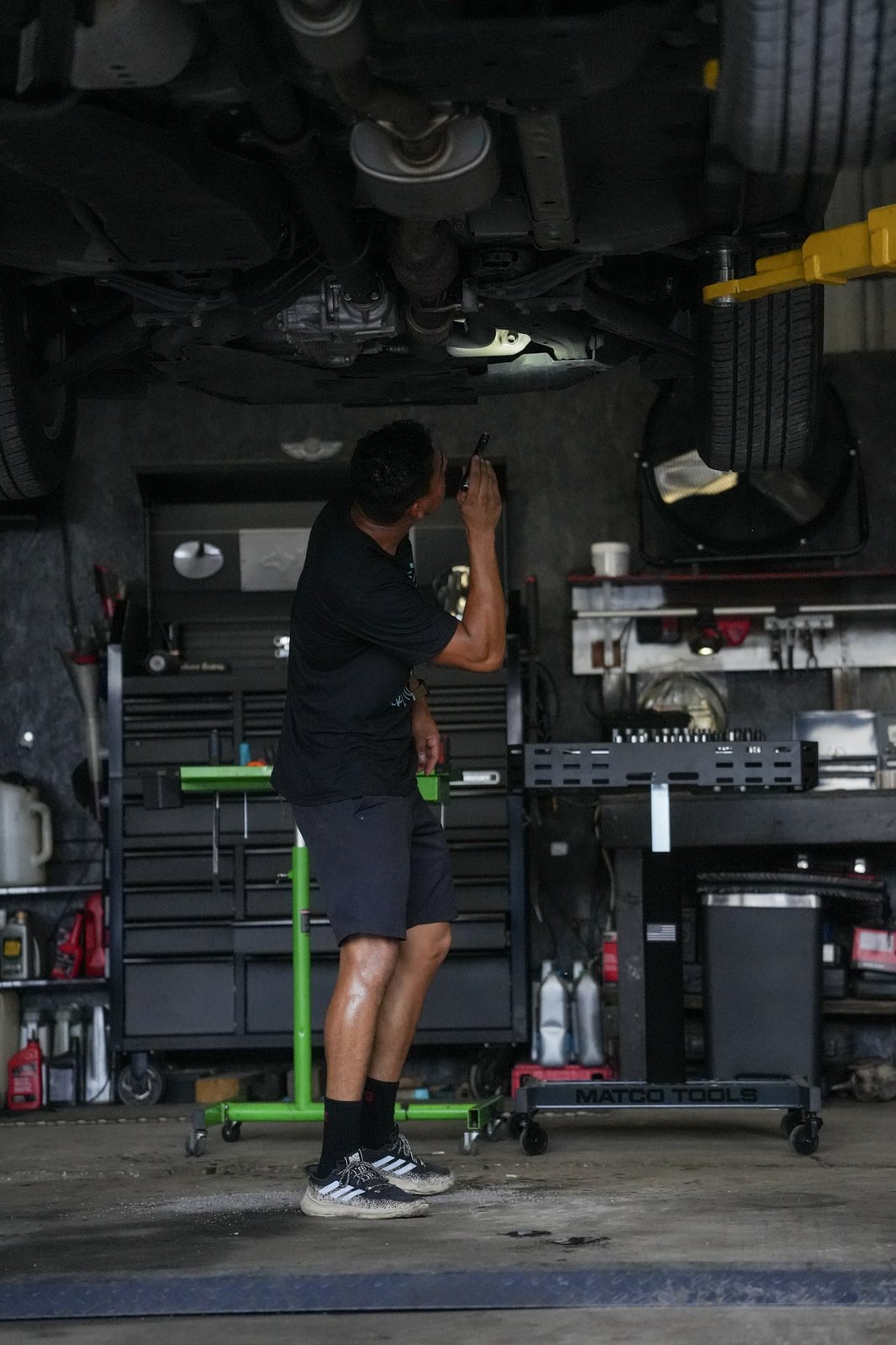 A mechanic standing under a vehicle on a lift, reaching up