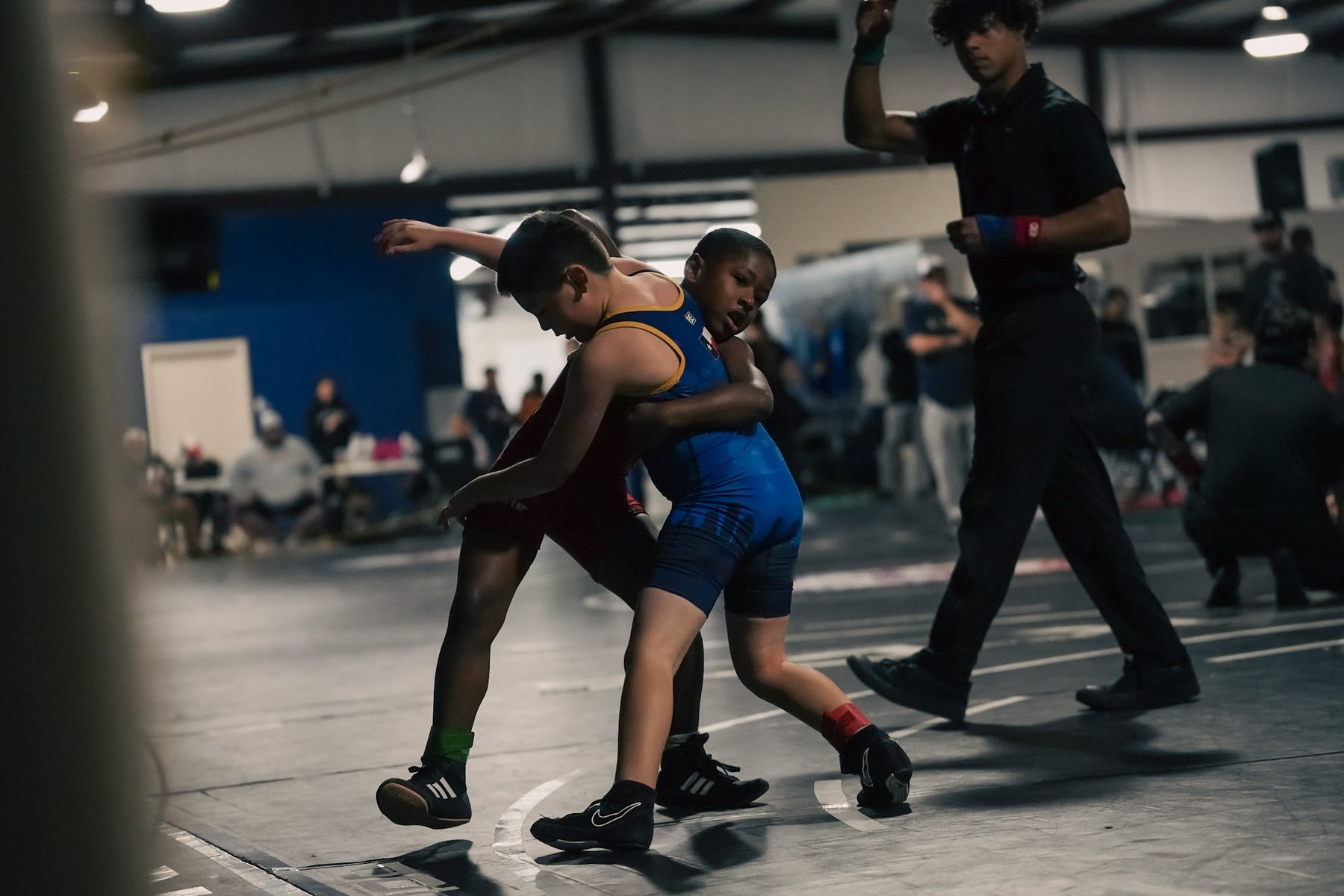 Two youth wrestlers grappling while the referee watches