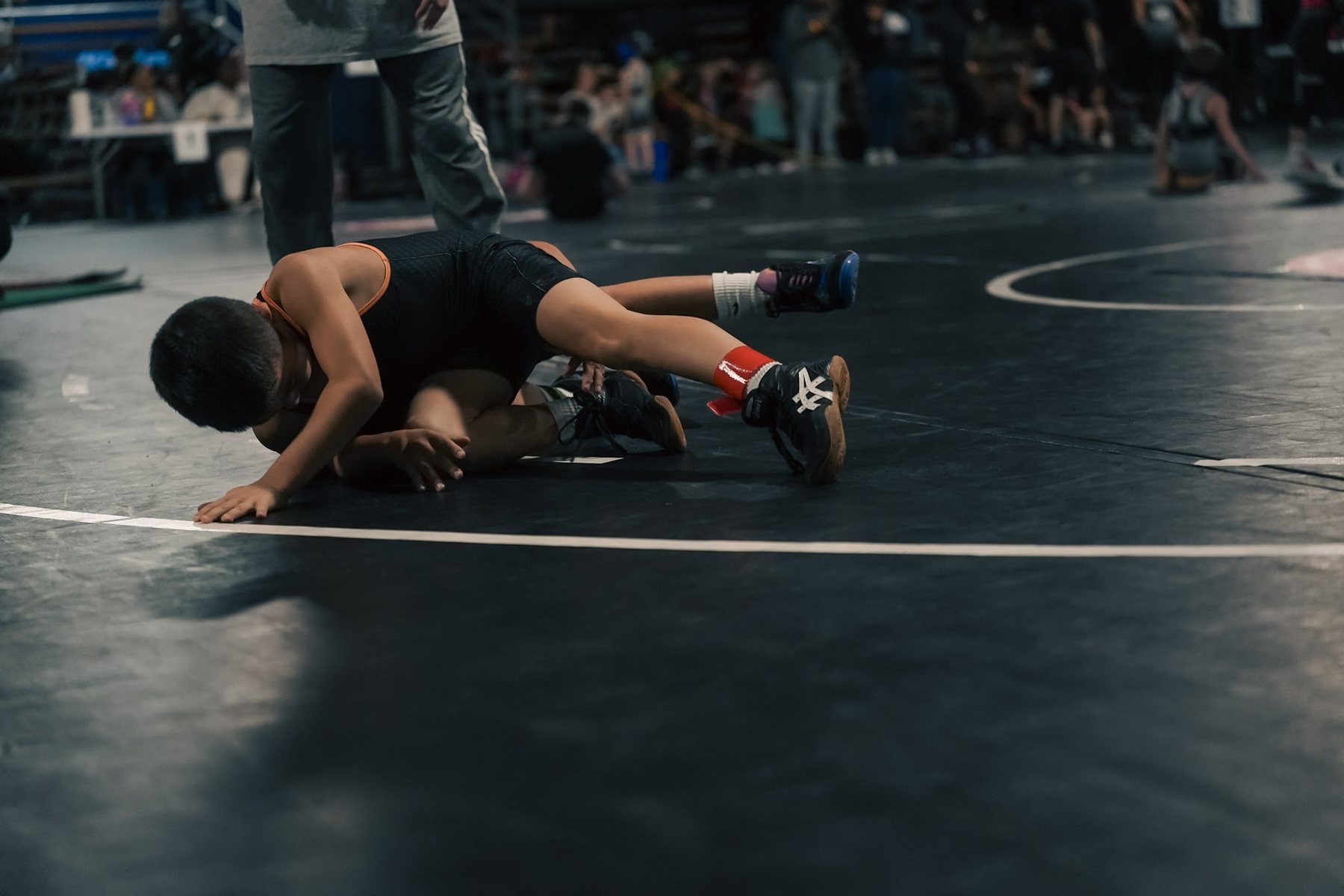 A youth wrestler driving through a takedown on a dark mat