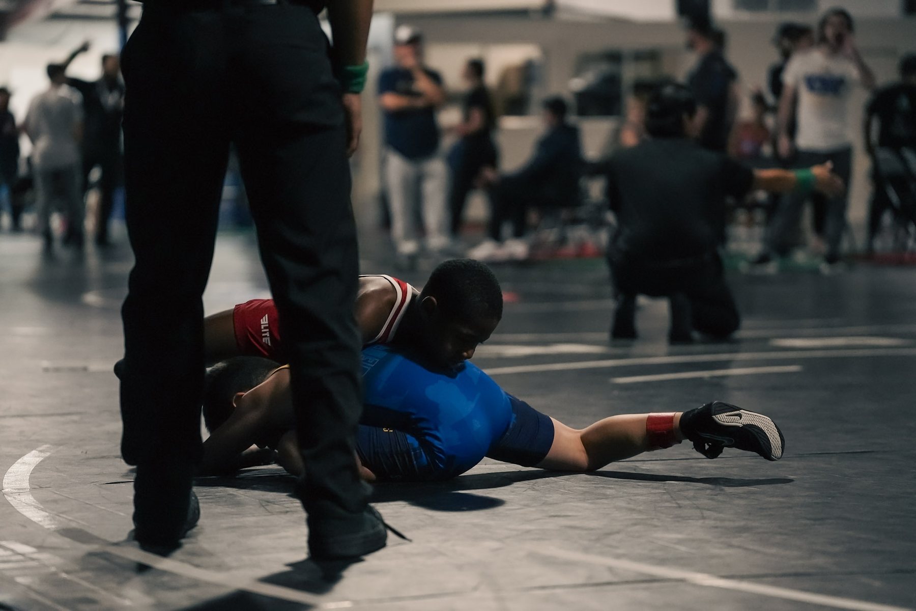 A youth wrestler pinning an opponent, seen past the referee&rsquo;s legs